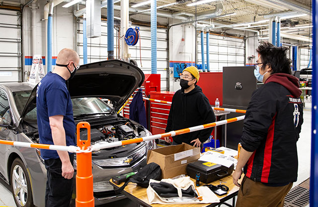 Students and instructor near car with open hood