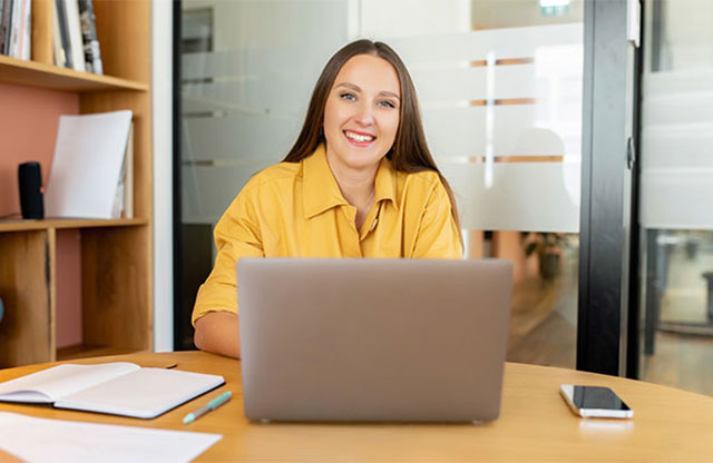 smiling person in yellow shirt in office on laptop