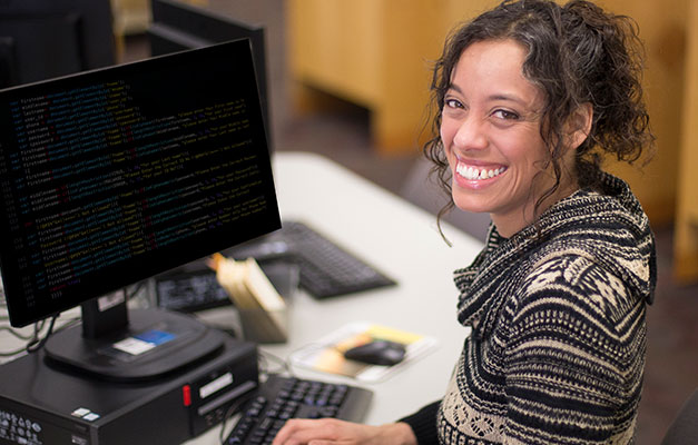 A Student Smiling at the Camera While Working on a Computer. 