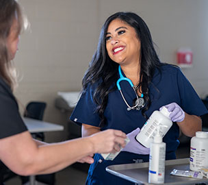 smiling student in navy scrups and gloves holding medication bottle
