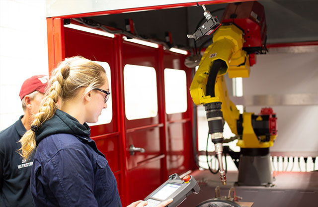 Student at laser welding machine with instructor over shoulder