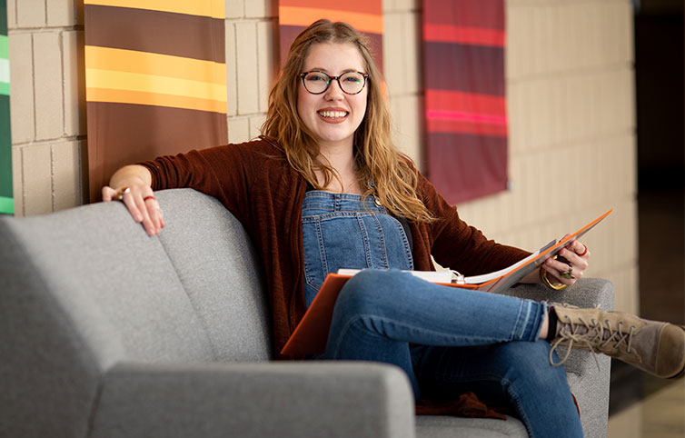 Student Sitting on the Couch in the Lobby with Study Materials and Looking at the Camera