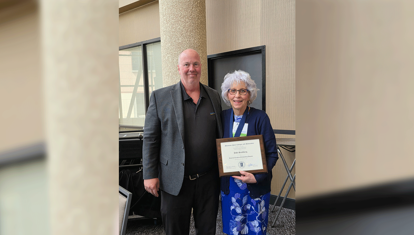 Two individuals standing next to each other, one holding an award.