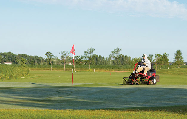 man in sweatshirt on a lawnmower at a golf course