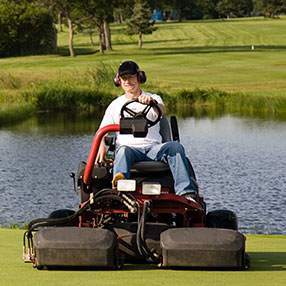 man in black hat on commercial lawn mower on golf course